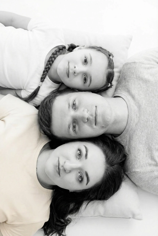 На основе предложенных фотографий, создай чёрно-белый профессиональный студийный портрет для этих людей, снятый сверху (top-down, overhead shot). Сохрани настоящие лица, возраст и индивидуальные черты людей.
Композиция «снизу вверх», шахматный порядок:
﻿﻿самый старший человек находится внизу, как мягкая подушка, его голова опирается на нейтральную студийную поверхность (например, плед или подушка);
следующие люди аккуратно и легко расположены на старшем человеке в шахматном порядке, их голова слегка приподнята, без ощущения давления; ﻿﻿

Несмотря на шахматное расположение, головы выстроены строго в одну вертикальную линию, взгляд в камеру.
Расположи их по убыванию возраста.

Видны только головы и плечи. Выражения мягкие, спокойные, нежные. Одежда однотонная, светлая или нейтральная, элегантная, без чёрного цвета.
Фон - чистый студийный, без пола и лишних деталей, создающий эффект «воздушного» портрета.
Стиль и освещение:
Студийная высококачественная чёрно-белая фотография (high-key).
Мягкий ровный свет сверху, минимум теней. Чистый фон; фотореализм, высокая детализация лиц, аккуратная текстура кожи; 8K.
