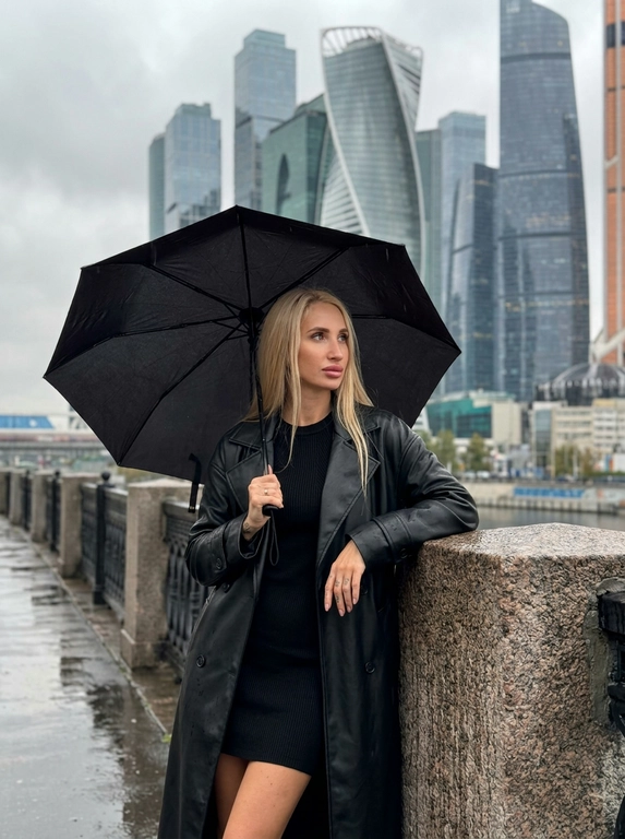 Городской портрет. Женщина у каменного ограждения на фоне башен «Москва-Сити». Корпус и тело женщины повернуты прямо к камере. Женщина стоит у современного каменного ограждения, строго опершись на него правым локтем и смотря в сторону-вправо. В левой руке раскрытый чёрный зонт, женщина находится под зонтом.

Фон: за спиной возвышаются небоскрёбы делового центра «Москва-Сити» под пасмурным дождливым небом. Вокруг холодная осенняя атмосфера. Мягкий рассеянный свет подчёркивает текстуру камня и грани стеклянных башен. Стиль lifestyle-блога.

Камера: объектив 85mm, f/2.2, ISO 100, RAW. Звенящая резкость на волосах, каменном парапете и ресницах. Visible pores, no plastic skin, no AI smoothing.

Запрет: каких-либо металлических поручней и перил.

Одежда: Лаконичное вязаное чёрное мини-платье по фигуре. Сверху длинное чёрное кожаное пальто свободного кроя, расстёгнутое.
