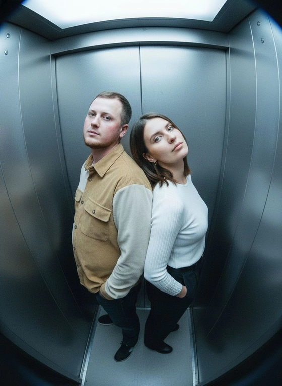 Используй предоставленные изображения и создай фото с двумя людьми в лифте с металлическими стенами. Цветовая гамма с преообладанием серых металлических оттенков. Кадр снят с максимально верхнего ракурса, люди будто заглядывают в камеру, их головы подняты наверх, взгляд в камеру. Легкий эффект fish eye. Реалистичное фото. Зернистость пленочного фото, насыщенные цвета, стиль фото y2k. Сохрани черты лица людей. Они стоят спиной друг к другу. Руки в карманах.
