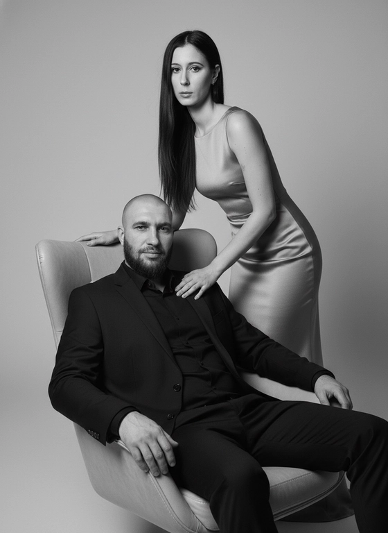 Глянцевая чёрно-белая фотосессия пары в студии. Мужчина расслабленно сидит в кресле, женщина элегантно склоняется над ним. Мягкий рассеянный свет, акцент на текстуре одежды и чертах лиц. Композиция сбалансирована, фон нейтральный. Стиль — high-fashion, как для обложки журнала.»
Сохранить внешность человека с исходного фото 