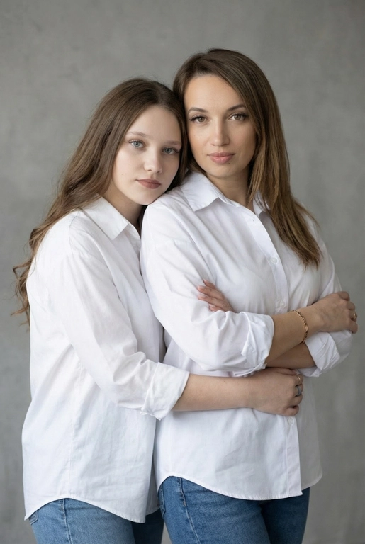 Используй эти два фото мамы и дочери и создай для них студийный портрет в чистом и элегантном стиле. Они стоят рядом, очень близко друг к другу. Дочь мягко обнимает маму за руку и слегка к ней прижимается со спины. Мама сложила руки перед грудью. Образ минималистичный, современный и стильный. На руке у матери тонкий золотой браслет. Профессиональный макияж и прическа.  Не менять черты лица ни на 1 процент. Фон — нейтральный серый с мягкой текстурой. Освещение рассеянное, мягкое, подчёркивающее естественные тона кожи. Атмосфера тёплая, нежная и спокойная, в стиле журнальной съёмки. Обе в свободных стильных белых рубашках с подвернутыми рукавами и джинсах.