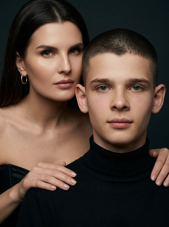 Гиперреалистичный студийный fashion-портрет молодой пары по загруженному референсу, 100% сходство лиц. Черты лица не изменять. Крупный план, кадр по плечи. Мужчина, спокойный уверенный взгляд прямо в камеру, естественное выражение лица, одет в черный трикотажный свитер с высоким воротом. Женщина стоит позади мужчины и нежно обнимает его, ее руки лежат на его плечах. Ее лицо расположено рядом с его лицом, она повернута слегка боком, голова немного наклонена вперед, взгляд направлен прямо в камеру. У женщины выразительные глаза с длинными густыми черными ресницами, естественный clean-glam макияж, натуральные брови, теплый оливковый оттенок кожи, небольшие серьги-кольца. Композиция плотная и интимная, их лица расположены очень близко друг к другу, современный модный портрет пары. Женщина одета в черный корсет. Кожа максимально натуральная: живая текстура кожи, видимые микропоры, subtle skin glow, естественный мягкий блеск кожи, natural skin microtexture, skin translucency, micro skin details, легкие естественные несовершенства кожи, без ретуши и без эффекта пластика. Освещение: мягкий студийный beauty lighting, рассеянный ключевой свет спереди и немного сбоку, мягкие глубокие тени для объема лица, деликатные световые блики на коже. Фон: глубокий темный студийный фон, темно-графитовый или почти черный, создающий контраст с кожей и лицами. Стиль: luxury fashion editorial photography, high fashion portrait, ultra photorealistic, 85mm portrait lens, shallow depth of field, creamy bokeh, cinematic soft lighting, RAW photo, extremely detailed, fine hair strands, natural skin pores, professional photography, photorealism, 8k, high dynamic range.