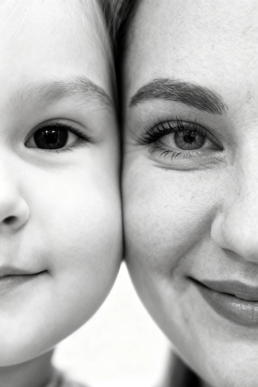 Сверхреалистичная черно-белая художественная фотография 8K женщины и ребенка, снятая очень крупным планом, щека к щеке так что видны только правая половина лица женщины и левая половина лица ребенка. которые смотрят в камеру. Их лица расположены рядом, почти соприкасаясь, образуя идеально сбалансированную симметричную композицию. Каждая деталь передана с фотографической точностью: тонкая текстура кожи и плавные градиенты света и тени. Видимая половина женщины включает ее бровь, один глаз , часть ее носа, щеку и губы, слегка приоткрытые в нежной, естественной улыбке, Видимая половина ребенка включает один глаз , круглую мягкую щеку, часть носа и небольшую улыбку, Фон белый и слегка размытый, что подчеркивает эмоциональную близость между ними. Освещение мягкое и рассеянное, создает деликатный контраст и тональную глубину. На снимке запечатлены нежность, близость и связь между матерью и ребенком, запечатленные с потрясающей реалистичностью. Не меняй черты лиц. 