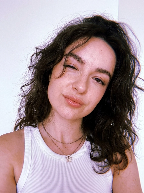 Vertical close-up portrait in the style of a natural selfie: a woman with her head tilted and a soft playful expression, one eye squinted or closed, gaze directed at the camera.
Expressive full lips, neat eyebrows, and soft makeup with an emphasis on the lips and eyes are noticeable on the face. There are thin chains around her neck, one with a small butterfly pendant.
The clothes are a white ribbed tank top with thin straps, revealing the shoulders and upper chest. The background is almost completely white, empty and minimalistic, like a light wall, without unnecessary objects.
The light is very soft, diffused, slightly overexposed, with a cool pink and purple hue, creating a gentle, slightly dreamy atmosphere.
The composition is close and intimate, the frame is cropped around the shoulders and chest, with emphasis on the face. The camera is at face level, creating the feeling of taking a picture from a phone. Light graininess, a gentle loss of detail in the highlights, natural, fashionable, slightly vintage aesthetic.



Причёска: Wavy hair, slightly tousled, with loose strands naturally falling across parts of the face without covering the eyes.