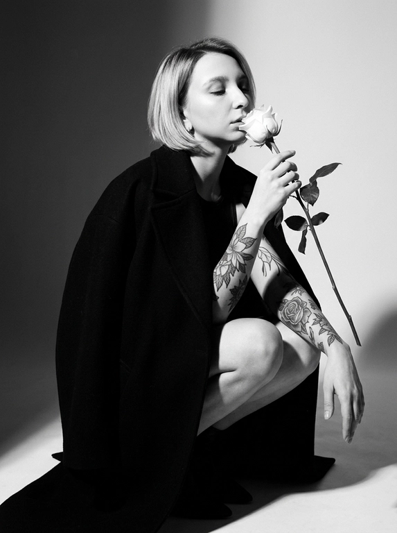 Высоко модная черно-белая редакционная фотография женщины в эффектной позе. Она грациозно присела на корточки, накинув на плечи объемное структурированное черное пальто, оставляя ноги открытыми.
Держит в руке белую розу с длинным стеблем и листьями, поднося к губам бутон. Изящный, минималистичный стиль. Сильное направленное студийное освещение, создающее глубокие тени и высокий контраст. Изысканный макияж с четкой подводкой для глаз и блеском на губах. Чистый фон, эстетика роскошного журнала, стиль Vogue, сверхчеткая, высококонтрастная монохромная фотография. Не изменяйте и не модифицируйте структуру лица, тон кожи или пропорции тела модели.
Только освещение, фон и застывшие текстуры должны быть переосмыслены в контексте задания. Сверхчеткое изображение, высокий динамический диапазон, студийная четкость, реалистичная текстура кожи, естественные поры, едва заметная зернистость пленки, редакционная цветокоррекция, съемка для печати.

Какая будет прическа?: Не изменять мою прическу.