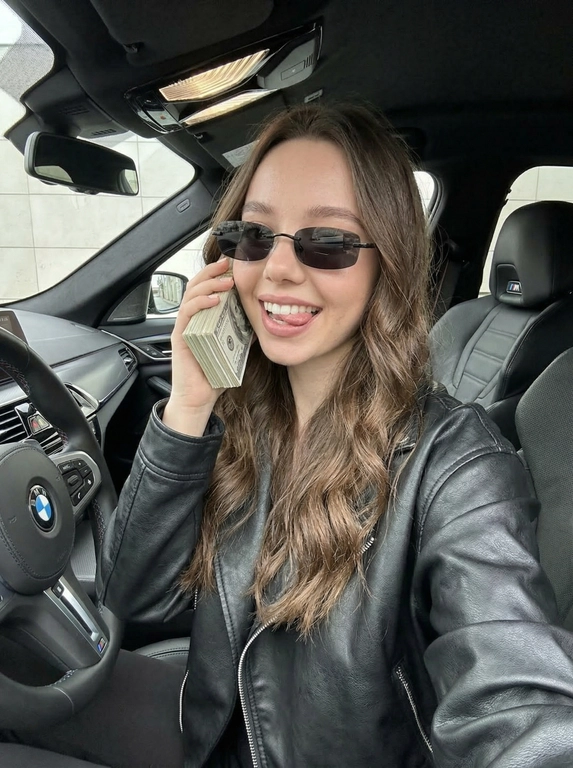 ultra realistic candid iPhone selfie photo use face from reference
EXACT 1:1 identity locked no changes skin clean flawless smooth beautiful even real natural texture NO depth of field NO background blur everything sharp like real phone camera medium close-up framing from chest up shot inside BMW M5 driver seat handheld slightly tilted natural angle woman sitting in driver seat body slightly leaned to the right head tilted slightly direct gaze into camera playful confident expression tongue slightly out lips with clear gloss and darker contour one hand holding a thick stack of US dollar bills pressed to ear like a phone fingers visible natural grip outfit oversized black leather biker jacket kosuha style structured shoulders visible seams glossy leather texture detailed folds sunglasses narrow oval rimless black lenses sleek minimal design covering eyes hair with natural structure airy volume straight cascade falling naturally to one side visible separated strands some strands near face not flat not glued lighting soft even ambient light subtle highlights on leather and sunglasses balanced exposure no harsh shadows color palette dark tones black outfit contrasting with green-white dollar bills modern sharp aesthetic boss attitude glamorous edgy mood texture visible fine grain micro-noise realistic iPhone processing