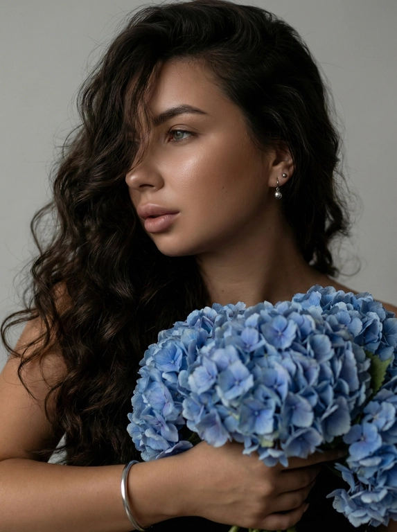   
Создайте ультрареалистичный портрет, не меняя черты лица.  крупным планом 3/4 с мягкой и освещенной загорелой кожей, атласной отделкой и естественным блеском, где женщина в профиле . Супер длинные волнистые  волосы, которые покрывают часть лица с объемными локонами,
выпадающими на лицо и плечо. Спокойное и чувственное выражение лица, а губы слегка полуоткрыты. Она носит серебряные серьги-шары и простой серебряный браслет на запястье. держит в руках огромный букет голубых гортензий. Фон нейтральный в светло-сером тоне, с темным и целенаправленным низким угловым освещением, которое улучшает контур лица, контур кожи и объем волос. Стиль редактирования красоты высокой моды, четкий фокус 8K, реалистичная текстура
изысканная и элегантная атмосфера.