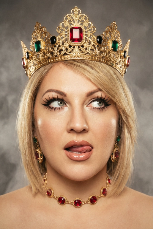 Создай фото -детальное описание художественного портрета девушки, выполненного в популярной современной эстетике, сочетающей элементы «е-qirl» и стиля «rebellious royalty» (бунтарская королевская особа).
:Центральный образ и внешность:
• Лицо и поза: Девушка позирует в дерзкой и провокационной манере.
Её глаза закатаны (или направлены сильно в сторону и вверх), а кончик языка слегка высунут. Это создает образ, сочетающий в себе игривость, бунт и некоторую отрешенность.
Элегантный макияж глаза с длинными острыми черными стрелками, длинные густые ресницы эффект лучики, нижние ресницы накрашены, хайлайтер во внутренних уголках и скулах.
Пухлые полностью прокрашенные телесной матовые губы слегка приоткрыты легкий блеск и светло-коричневый карандаш по краям. персиково-розового оттенка.
Не меняй мою прическу. 
Корона: На голове массивная высокая корона в винтажном стиле. Она украшена сложным филигранным узором и крупными драгоценными камнями: по центру расположен большой квадратный красный камень (рубин), по бокам - камни зеленого (изумруд) и черного цветов. Корона сидит немного небрежно, подчеркивая неформальность образа.
Ожерелья:
На шее надет чокер, выполненный в одном стиле с короной - цепочка с круглыми красными камнями в оправе. В ушах серьги по такому же типо как корона •
Фон: Нейтральный, дымчато-серый или слегка туманный. Он лишен деталей, что позволяет полностью сфокусировать внимание на ярких аксессуарах и лице модели.
Освещение и обработка: Свет мягкий, рассеянный. Фотография имеет характерную обработку с эффектом «зернистости» (пленочное зерно), что придает ей винтажный и художественный вид.
Цветовая гамма теплая, с акцентом на золото и красный цвет.
Общее впечатление:
Снимок транслирует идею современной интерпретации власти и красоты. Это противопоставление классического символа величия (короны) и современного неформального поведения.
Образ выглядит стильно и кинематографично и запоминающе, сильная вспышка. Корона цвета золота.