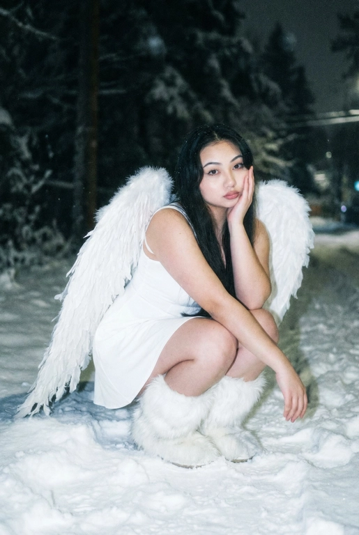  Создай фото человека на основе загруженной фотографии.
Белое платье без рукавов, пушистые белые сапоги, большие белые крылья, опущенные вниз, шире плеч.
Сидит на корточках на снегу, рукой касается щеки. На заднем плане заснеженный лес.
Ночная улица, тёмный размытый фон, вспышка.
Мягкое нечеткое фото: шум, зерно, лёгкое размытие, холодная атмосфера.