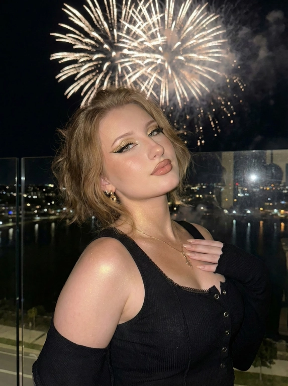   Создай не меняя черты лица.Мобильная съемка на айфон 15 pro, со вспышкой. Ночное время. Не меняя внешности женщины с фото, образ предстает в ярком, ночном освещении, резко выделяя её фигуру на фоне ночного неба, на котором по всему небу зажигаются салюты и освещают женщину . Портрет по пояс.
Женщина стоит полубоком, слегка наклонив голову и смотрит прямо в камеру с игривым, но уверенным выражением лица. Её волосы каре,темно-русого цвета, придавая образу лёгкость и динамику. Взгляд подчёркнут эффектным макияжем с акцентом на глаза и ресницы. Макияж: губы окрашены по контуру, заполнены глянцевой помадой нюдового цвета, на подвижных веках золотистый шиммер, черные стрелки, сверху них блестящие золотые стрелки, длинные ресницы, легкий румянец, золотой хайлайтер. На теле блестящий золотистый шиммер. Она одета в одежду с фото (приложила)
Высокая детализация кожи и пор.
Маникюр нюдовые ногти.золотые серьги и элегантное колье на шее.
Рука женщины частично закрыта рукавом, что создаёт ощущение уютной небрежности. Свет мягко играет на слегка загорелой коже, подчёркивая плавность линий плеч и КЛюЧиц, создавая лёгкие блики и тени, которые акцентируют естественную красоту тела. Общая атмосфера кадра наполнена камерной легкой загадочностью, гармоничным сочетанием непринуждённости с изысканностью, где каждая деталь - от фактуры одежды до макияжа и позы - работает на создание глубокого, эмоционального портрета на фоне ночного города, едва различимого за стеклянным ограждением. Эта сцена наполнена тихой энергией и эстетикой современного гламура, погружая зрителя в атмосферу вечернего отдыха на открытом воздухе с лёгким намёком на таинственность, фотореалистичное изображение, высокая текстурная детализация, высокое качество.