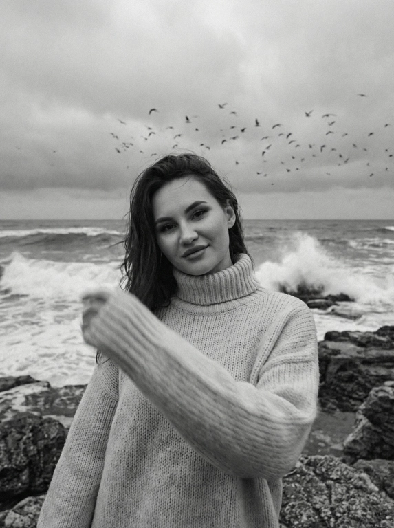 Создай портрет, не меняя черты лица. Черно-белая фотография в стиле ретро: человек стоит на морском побережье, в полупрофиль, смотрит нежно в камеру, легкая улыбка на лице, одет(а) в светлый оверсайз вязаный свитер с высоким воротником. На переднем плане — размытая рука в движении (motion blur), на заднем плане — море с волнами и стая птиц в небе, пасмурное небо. Сильная зернистость пленки, винтажная эстетика, атмосфера свободы, эффект размытия в движении, эстетика.



