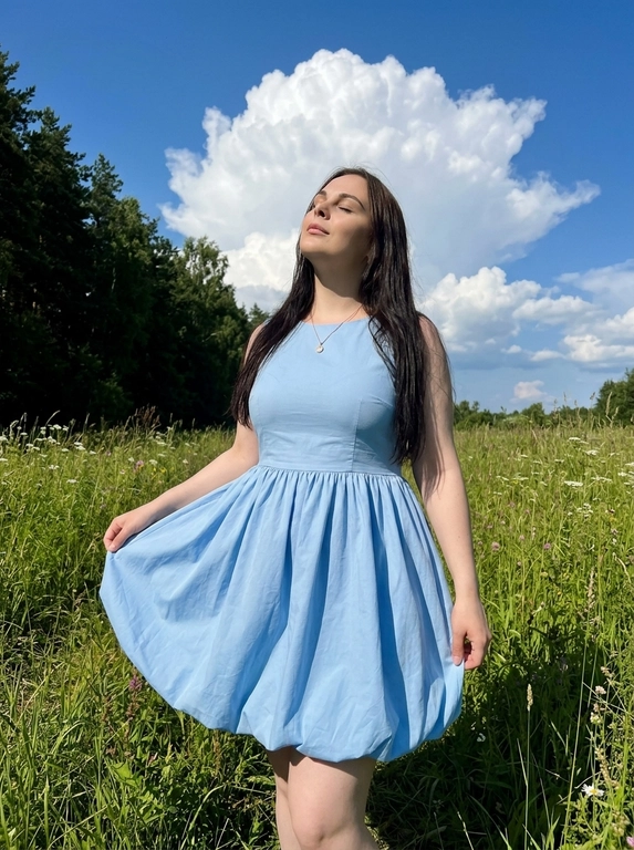 Фотореалистичное фото как из Pinterest, снято на заднюю камеру смартфона , обычный режим, без портретного режима, вертикальный кадр , натуральная экспозиция, реалистичная резкость смартфона, лёгкое естественное зерно. Без ИИ‑ретуши, без ИИ‑масок, без «пластика», без замыливания, без бьюти‑фильтров, без HDR, без агрессивного шумоподавления , видна естественная текстура кожи, ткани и травы. 
Локация: летний луговой склон с высокой зелёной травой и белыми полевыми цветами , слева тёмная кромка леса, густые деревья, вдали небольшой холм. Над головой яркое синее небо с крупным объёмным белым кучевым облаком, солнечный день.
Свет: жёсткий дневной солнечный свет сверху или сбоку, контрастные тени на траве, выраженные солнечные блики на плечах и ключицах, без пересветов.
ракурс: съёмка с уровня талии или чуть ниже, средний план примерно от середины бёдер и выше с большим количеством неба в кадре, акцент на фигуре на фоне облаков. Фокус на модели, фон слегка мягкий и  естественный, без искусственного боке.
Поза: модель стоит в траве, голова запрокинута вверх, глаза закрыты, лицо повернуто к солнцу, расслабленное мечтательное настроение. Одна рука держит край юбки, вторая опущена вдоль бедра. Минималистичные украшения: тонкая цепочка с небольшим кулоном.
Естественный макияж, натуральная кожа без глянца и без сглаживания. 

Какое будет платье?: На модели светло-голубое платье-баллон современного кроя: лаконичный приталенный верх, чистая линия плеч, объёмная округлая юбка с мягким подолом, плотная матовая ткань, fashion-силуэт без лишнего декора.