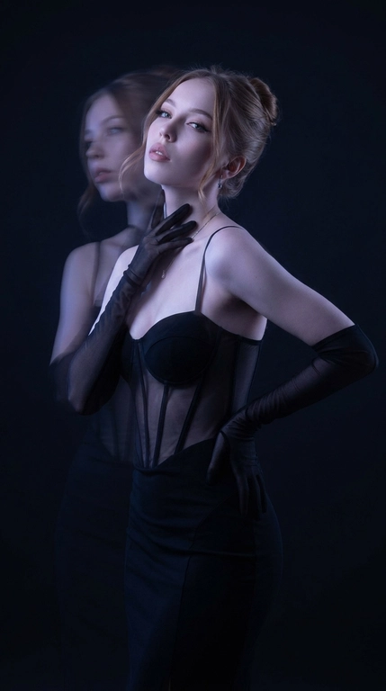 Фотореалистичный fashion-портрет. Женщина стоит вполоборота к камере, корпус плавно изогнут в S-образной линии, одно плечо слегка опущено вперёд, подбородок приподнят. Одна рука поднята к шее и линии ключицы, кончики пальцев мягко касаются области под подбородком, вторая рука согнута в локте и лежит на талии сбоку, локоть отведён в сторону. Голова слегка наклонена назад и в сторону, взгляд направлен на объектив, выражение лица чувственное, уверенное и загадочное.

Тёмная студия практически растворяется в глубоких тенях. Основная фигура остаётся резкой, рядом появляется полупрозрачный смещённый силуэт, создающий эффект двойной экспозиции и призрачного движения. Фон остаётся чистым и тёмным, без световых полос и линий.

Очень низкий ключ освещения, глубокие чёрные тени, минимальное количество света, акцентное холодное освещение по контуру лица, плеч и фигуры, большая часть кадра погружена в полумрак.

Цветокоррекция в стиле мрачной luxury fashion-съёмки: почти чёрный фон, холодные сине-фиолетовые оттенки, высокий контраст, приглушённые света, глубокие бархатные тени, эффект длинной выдержки, motion blur, художественная двойная экспозиция, кинематографичная атмосфера дорогой редакционной съёмки для Vogue, объектив 85mm, f/1.8, высокая детализация, премиальная студийная фотография.


Какая будет прическа?: Волосы собраны в элегантную вечернюю причёску, аккуратно поднятую наверх или назад, с мягким чистым силуэтом. У лица выпущены несколько тонких мягких прядей, которые деликатно обрамляют скулы и линию подбородка, добавляя образу утончённость и чувственность.

Какая будет одежда?: На женщине облегающее корсетное чёрное платье с полупрозрачными вставками на талии. Образ дополняют длинные полупрозрачные чёрные перчатки и минималистичные украшения. Силуэт выглядит чувственно, драматично и в эстетике высокой моды.

Доп. характеристики: Цвет глаз зеленый, волосы прямые светло-русые длинные