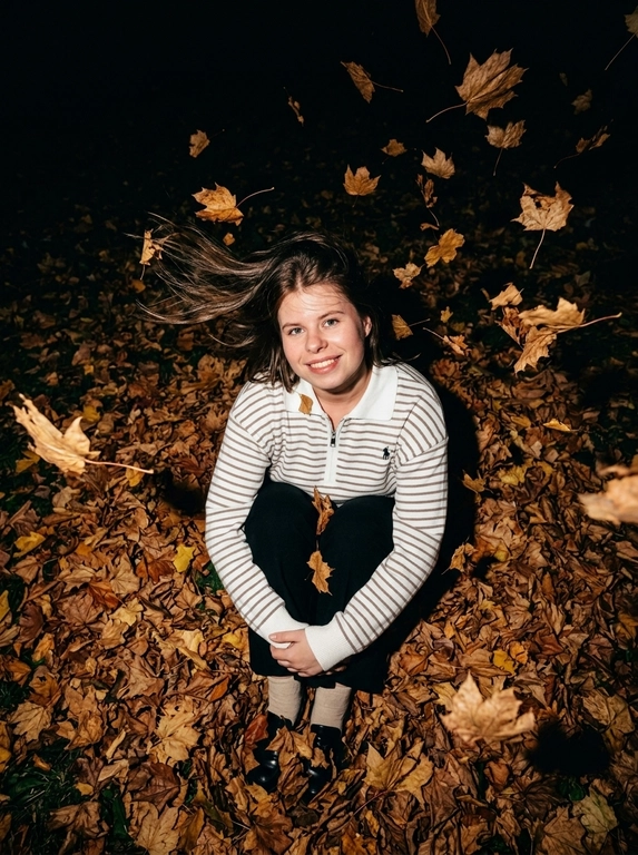 Ultra-realistic candid NIGHT autumn photo. The woman sits curled up directly in a thick carpet of dry autumn maple leaves, knees pulled toward her chest. Camera positioned very high above her, almost directly overhead, dramatic top-down perspective. She raises her face toward the camera, one hand gently supporting her cheek, the other arm resting across her knees.
She wears a fitted white knitted top with very long dramatic FLARED BELL SLEEVES, fitted through the arms and strongly widening from the elbows.
Strong autumn wind blows her hair.

It is DARK outside, almost nighttime. The background beyond the flash falls into deep natural darkness. Shot with a powerful direct on-camera flash: her face, white sweater and the closest leaves are brightly illuminated, while distant leaves rapidly disappear into black shadows. Dozens of dry orange, rust and brown leaves are FLYING THROUGH THE AIR around her, caught mid-flight by the flash; some pass very close to the lens and create strong realistic motion blur and streaks. A few strands of hair also have motion blur from the wind. Face remains sharp. Raw spontaneous flash photography, high contrast, deep blacks, warm saturated autumn tones, slight grain, imperfect handheld framing, realistic textures, no studio lighting, no HDR, no AI look.