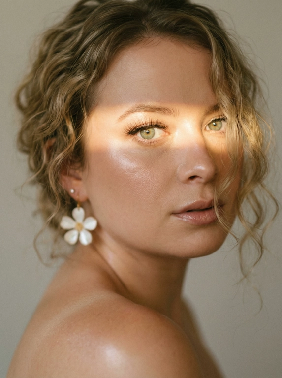 Кинематографический эффект с добавлением зерна. Ультрареалистичный, экстремально крупный портрет части лица девушки: на неё падает солнечный свет полосой, освещая глаза; её голова немного повёрнута в сторону. Тело подсвечено хайлайтером. Макияж лёгкий, с насыщенным хайлайтером; ресницы длинные, пышные. Она смотрит в камеру со спокойным, созерцательным выражением. Освещение мягкое, с лёгким акцентом на её лицо, создаёт нежные тени и подчёркивает черты. В ушах — серьги в виде белых цветов. Фон минималистичный и нейтральный, что усиливает спокойную и элегантную атмосферу. Фото смазанное, как будто сделано в движении, с двойной экспозицией.


Какая будет прическа?: Волосы кудрявые, частично падают на лицо.