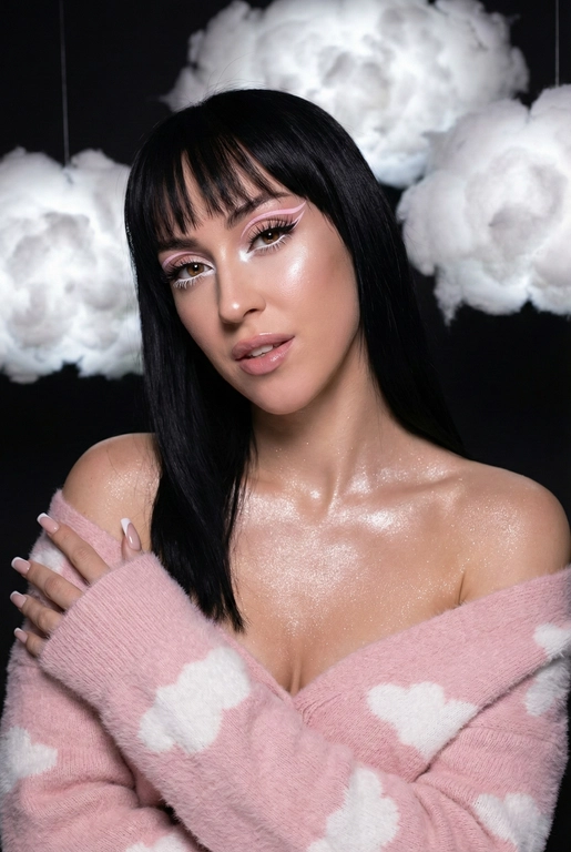 Крупный план лица девушки в стиле «высокой моды». Элегантный макияж глаза с длинными острыми нежно розовые двойные изогнутые стрелки, длинные густые ресницы эффект лучики, нижние густо ресницы накрашены белым и белый каял карандаш на нижнем веке белый Хайлайтер во внутренних уголках и скулах. Губы слегка приоткрыты в легкой ухмылке в легком блеске. Голова наклонена в сторону. На ней пушистый дорогой кашемировый нежно розовый свитер с белыми облаками плечи открыты.
За ней свисают объемные пушистые облака из ваты подсвеченные белым изнутри. Тело и декольте подсвечены хайлайтером и шиммером. Высокая детализация текстур кожи, одежды и волос. Черты лица-полностью сохранены как на референсном фото.
Ногти френч квадрат длинные.
На фоне светлая большая бьюти студия, вокруг темно, ее лицо освещено яркой лампой. Не менять свою прическу