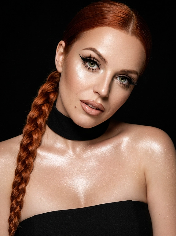 Крупный план лица женщины в стиле «высокой моды». Элегантный макияж: глаза с длинными острыми чёрными стрелками, длинные густые ресницы с эффектом «лучики», нижние ресницы также прокрашены. Хайлайтер во внутренних уголках глаз и на скулах. Губы слегка приоткрыты в лёгкой ухмылке, с лёгким блеском и светло-коричневым карандашом по контуру. Голова наклонена в сторону,  На ней чёрный топ из тканевого материала без бретелек. Тело и зона декольте подсвечены хайлайтером, на шее чёрная ткань. Высокая детализация текстур кожи, одежды и волос. Черты лица полностью сохранены, как на референсном фото. Фон чёрный, студийный, вокруг темнота, лицо освещено яркой лампой. 8K, тёмный минималистичный фон без лишних деталей. Гиперреализм, добавить зерно.

Какая будет прическа?: Волосы заплетены в длинную косу