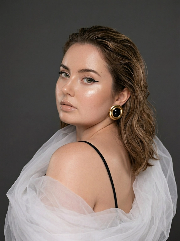 Это студийный портрет женщины, выполненный в гламурном стиле. Фон темно-серый, практически нейтральный. Освещение акцентирует внимание на лице и плечах, создавая глянцевый эффект. 

Одежда минималистична: видна лишь тонкая черная бретелька. Акцент сделан на массивные серьги в винтажном стиле – круглые, с черным камнем в золотой оправе. На плече и частично на спине – объемная деталь из полупрозрачной белой ткани, похожей на тюль или органзу, создающая эффект облака или крыла.

Поза женщины – полуоборот, взгляд направлен поверх плеча в камеру. Лицо повернуто чуть вбок, что подчеркивает скулы. Прическа – волосы зачесаны назад и уложены волнами, создавая эффект влажных волос. Макияж яркий: акцент на глаза с четкими черными стрелками, сияющие хайлайтер скулы и глянцевые губы.

Атмосфера снимка – элегантность и чувственность. Цветовая гамма – приглушенные тона с акцентом на теплые оттенки кожи и золотистые детали.