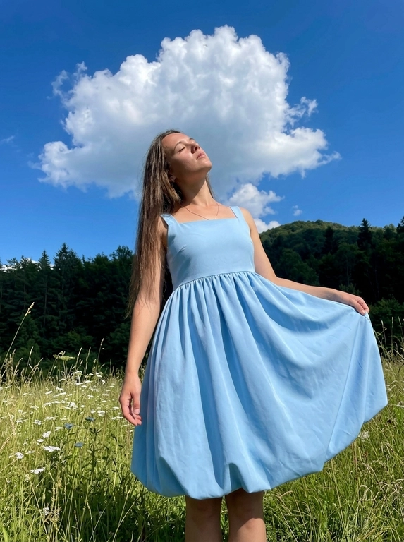 Фотореалистичное фото как из Pinterest, снято на заднюю камеру смартфона , обычный режим, без портретного режима, вертикальный кадр , натуральная экспозиция, реалистичная резкость смартфона, лёгкое естественное зерно. Без ИИ‑ретуши, без ИИ‑масок, без «пластика», без замыливания, без бьюти‑фильтров, без HDR, без агрессивного шумоподавления , видна естественная текстура кожи, ткани и травы. 
Локация: летний луговой склон с высокой зелёной травой и белыми полевыми цветами , слева тёмная кромка леса, густые деревья, вдали небольшой холм. Над головой яркое синее небо с крупным объёмным белым кучевым облаком, солнечный день.
Свет: жёсткий дневной солнечный свет сверху или сбоку, контрастные тени на траве, выраженные солнечные блики на плечах и ключицах, без пересветов.
ракурс: съёмка с уровня талии или чуть ниже, средний план примерно от середины бёдер и выше с большим количеством неба в кадре, акцент на фигуре на фоне облаков. Фокус на модели, фон слегка мягкий и  естественный, без искусственного боке.
Поза: модель стоит в траве, голова запрокинута вверх, глаза закрыты, лицо повернуто к солнцу, расслабленное мечтательное настроение. Одна рука держит край юбки, вторая опущена вдоль бедра. Минималистичные украшения: тонкая цепочка с небольшим кулоном.
Естественный макияж, натуральная кожа без глянца и без сглаживания. 

Какое будет платье?: На модели светло-голубое платье-баллон современного кроя: лаконичный приталенный верх, чистая линия плеч, объёмная округлая юбка с мягким подолом, плотная матовая ткань, fashion-силуэт без лишнего декора.