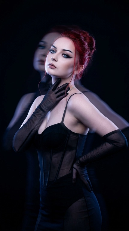 Фотореалистичный fashion-портрет. Женщина стоит вполоборота к камере, корпус плавно изогнут в S-образной линии, одно плечо слегка опущено вперёд, подбородок приподнят. Одна рука поднята к шее и линии ключицы, кончики пальцев мягко касаются области под подбородком, вторая рука согнута в локте и лежит на талии сбоку, локоть отведён в сторону. Голова слегка наклонена назад и в сторону, взгляд направлен на объектив, выражение лица чувственное, уверенное и загадочное.

Тёмная студия практически растворяется в глубоких тенях. Основная фигура остаётся резкой, рядом появляется полупрозрачный смещённый силуэт, создающий эффект двойной экспозиции и призрачного движения. Фон остаётся чистым и тёмным, без световых полос и линий.

Очень низкий ключ освещения, глубокие чёрные тени, минимальное количество света, акцентное холодное освещение по контуру лица, плеч и фигуры, большая часть кадра погружена в полумрак.

Цветокоррекция в стиле мрачной luxury fashion-съёмки: почти чёрный фон, холодные сине-фиолетовые оттенки, высокий контраст, приглушённые света, глубокие бархатные тени, эффект длинной выдержки, motion blur, художественная двойная экспозиция, кинематографичная атмосфера дорогой редакционной съёмки для Vogue, объектив 85mm, f/1.8, высокая детализация, премиальная студийная фотография.


Какая будет прическа?: Волосы собраны в элегантную вечернюю причёску, аккуратно поднятую наверх или назад, с мягким чистым силуэтом. У лица выпущены несколько тонких мягких прядей, которые деликатно обрамляют скулы и линию подбородка, добавляя образу утончённость и чувственность.

Какая будет одежда?: На женщине облегающее корсетное чёрное платье с полупрозрачными вставками на талии. Образ дополняют длинные полупрозрачные чёрные перчатки и минималистичные украшения. Силуэт выглядит чувственно, драматично и в эстетике высокой моды.