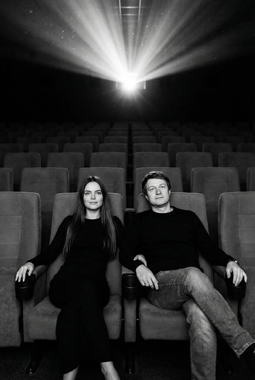  Кинематографичный чёрно-белый портрет пары в пустом кинозале.
Женщина и мужчина сидят рядом в мягких креслах кинотеатра.
кадр с глубоким пространством и пустыми рядами кресел позади них. Женщина черном длинном обтягивающем платье, поза женственная и спокойная, одна рука на подлокотнике.
Мужчина в черном свитере и в джинсах, сидит расслабленно.
Над ними яркий луч проектора, и выразительные блики.