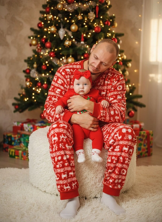 Лицо мужчины и ребенка не менять ,оставить без изменений .
Мужчина в красной новогодней пижаме держит на руках девочку в новогоднем красном Боди с белыми носочками с сердечками ,на голове у ребенка красная появязка с бантом ,мужчина сидит на махровом белом кофре ,сзади новогодняя ель с подарками  