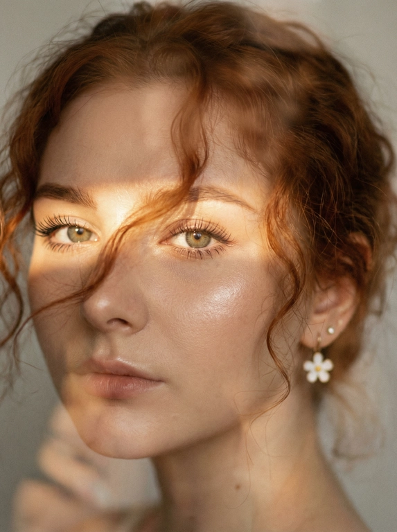 Кинематографический эффект с добавлением зерна. Ультрареалистичный, экстремально крупный портрет части лица девушки: на неё падает солнечный свет полосой, освещая глаза; её голова немного повёрнута в сторону. Тело подсвечено хайлайтером. Макияж лёгкий, с насыщенным хайлайтером; ресницы длинные, пышные. Она смотрит в камеру со спокойным, созерцательным выражением. Освещение мягкое, с лёгким акцентом на её лицо, создаёт нежные тени и подчёркивает черты. В ушах — серьги в виде белых цветов. Фон минималистичный и нейтральный, что усиливает спокойную и элегантную атмосферу. Фото смазанное, как будто сделано в движении, с двойной экспозицией.


Какая будет прическа?: Волосы кудрявые, частично падают на лицо.