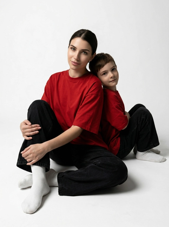 Гиперреалистичная фотография. Качество 8К. Используя портретное сходство с людьми с фотографий, создай фотографию: женщина в красной оверсайз свободной футболке и свободных черных джинсах, белых носках. Ребенок одет в красную оверсайз футболку, черные свободные джинсы и белые носочки. Женщина сидит на полу, согнув колени, смотрит прямо в кадр с еле заметной улыбкой. Сзади женщины в такой же позе сидит ребенок облокотившись спиной к спине женщины, с легкой улыбкой. Темный стиль модного редакционного журнала, глубокие тени и драматическое студийное освещение, белый фон, элегантная и мощная композиция, ультрареалистичный, высокая детализация, художественный портрет.
