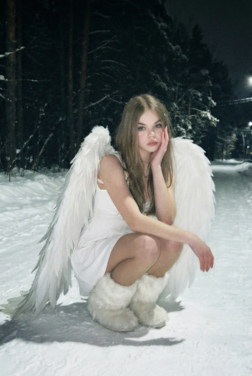  Создай фото человека на основе загруженной фотографии.
Белое платье без рукавов, пушистые белые сапоги, большие белые крылья, опущенные вниз, шире плеч.
Сидит на корточках на снегу, рукой касается щеки. На заднем плане заснеженный лес.
Ночная улица, тёмный размытый фон, вспышка.
Мягкое нечеткое фото: шум, зерно, лёгкое размытие, холодная атмосфера.