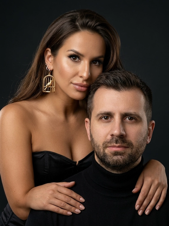 Гиперреалистичный студийный fashion-портрет молодой пары по загруженному референсу, 100% сходство лиц. Черты лица не изменять. Крупный план, кадр по плечи. Мужчина, спокойный уверенный взгляд прямо в камеру, естественное выражение лица, одет в черный трикотажный свитер с высоким воротом. Женщина с волосами цветом и длиной как на фото, мягкая боковая укладка. Она стоит позади мужчины и нежно обнимает его, ее руки лежат на его плечах. Ее лицо расположено рядом с его лицом, она повернута слегка боком, голова немного наклонена вперед, взгляд направлен прямо в камеру. У женщины выразительные глаза с длинными густыми черными ресницами, естественный clean-glam макияж, натуральные брови, нюдовые губы, теплый оливковый оттенок кожи, небольшие серьги-кольца. Композиция плотная и интимная, их лица расположены очень близко друг к другу, современный модный портрет пары. Девушка одета в черный корсет серьги из золота, большие, изображают птиц в золотых клетах. Кожа максимально натуральная: живая текстура кожи, видимые микропоры, subtle skin glow, естественный мягкий блеск кожи, natural skin microtexture, skin translucency, micro skin details, легкие естественные несовершенства кожи, без ретуши и без эффекта пластика. Освещение: мягкий студийный beauty lighting, рассеянный ключевой свет спереди и немного сбоку, мягкие глубокие тени для объема лица, деликатные световые блики на коже. Фон: глубокий темный студийный фон, темно-графитовый или почти черный, создающий контраст с кожей и лицами. Стиль: luxury fashion editorial photography, high fashion portrait, ultra photorealistic, 85mm portrait lens, shallow depth of field, creamy bokeh, cinematic soft lighting, RAW photo, extremely detailed, fine hair strands, natural skin pores, professional photography, photorealism, 8k, high dynamic range. Вертикальный формат 9:16 Негативный промт: ai plastic skin, wax skin, overly smooth skin, doll face, beauty filter, cgi, 3d render, overretouched skin, unrealistic skin texture, bad anatomy, distorted face, extra fingers, low detail, blurry skin, artificial texture, oversharpen, fake lighting