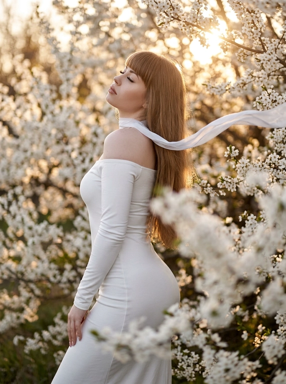 A woman standing among dense white blooming branches.
Side profile, body turned away, head tilted back upward toward the light, eyes closed.
Framing from mid-thigh to head.
Camera slightly below eye level, 85mm look.
Clothing:
Long white fitted dress with long tight sleeves and off-shoulder design (bare shoulders).
Accessory (CRITICAL):
A thin white ribbon scarf around her neck, very light fabric.
The ribbon flows in the wind and extends across the frame.
Flowers (CRITICAL):
Dense white blossoms surrounding the subject exactly like the reference.
Foreground flowers heavily blurred, partially covering bottom and right side.
Background filled with soft white blossoms and warm bokeh.
Lighting:
Golden hour sunlight from top right, strong warm backlight, glowing rim light on hair and shoulders, sun visible through branches.
Shallow depth of field, subject sharp, foreground/background soft.
Warm cinematic tones, soft highlights, photorealistic, high detail.