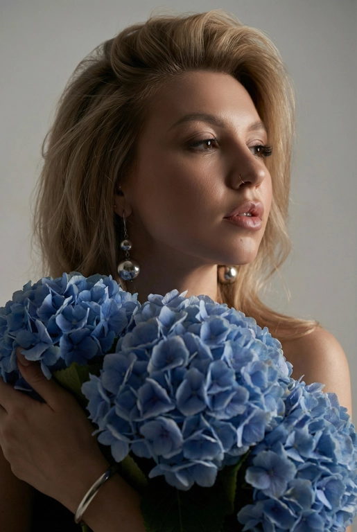Создайте ультрареалистичный портрет, не меняя черты лица, крупным планом 3/4, с мягкой, освещённой кожей, атласной отделкой и естественным блеском, где женщина изображена в профиле. Спокойное и чувственное выражение лица, губы слегка полуоткрыты. Она носит серебряные серьги-шары и простой серебряный браслет на запястье.
Фон нейтральный, в светло-сером тоне, с тёмным, целенаправленным низким угловым освещением, которое подчёркивает контур лица, текстуру кожи и объём волос. Стиль редактирования — высокая мода, чёткий фокус 8K, реалистичная текстура, изысканная и элегантная атмосфера.


Как на фото 

Цветы: Держит в руках огромный букет голубых гортензий