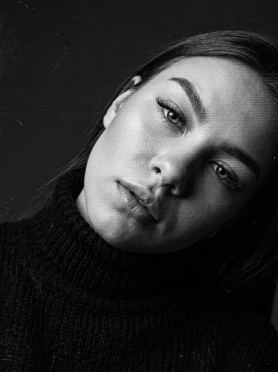 Крупный план (close-up), портрет. Угол: легкий наклон головы (Dutch angle), взгляд снизу вверх. Объектив: портретный (85mm). Глубина резкости: малая, фокус на глазах и губах. Фон: темный, однотонный, с эффектом аналоговых помех.
Голова сильно наклонена к плечу, создавая динамичную и чувственную композицию. Взгляд направлен в камеру, томный и глубокий. Губы слегка расслаблены и приоткрыты.
ВОЛОСЫ: слегка растрепанные.
Черный вязаный свитер с высоким воротником (водолазка). Видна грубая текстура вязки с мелкими ворсинками.
Контрастное студийное освещение (Chiaroscuro). Яркий источник света направлен сбоку, создавая глубокие тени и подчеркивая рельеф скул, носа и объем губ. Сильные блики на коже (highlight).
Черно-белое (B&W) изображение с глубоким черным цветом. Наложено стилизованное наложение в виде горизонтальных линий сканирования, имитирующих старый телевизионный сигнал или VHS-кассету. Присутствует эффект зернистости (film grain) и легкие царапины (dust and scratches).
Несмотря на стилизацию под VHS, сохранена высокая детализация: видна пористая текстура кожи, влажный блеск на губах, ворсинки на свитере и индивидуальные ресницы.
Стилизованное под «ретро-футуризм» или «dark aesthetic». Сочетание высокой четкости черт лица с намеренными цифровыми/аналоговыми искажениями.