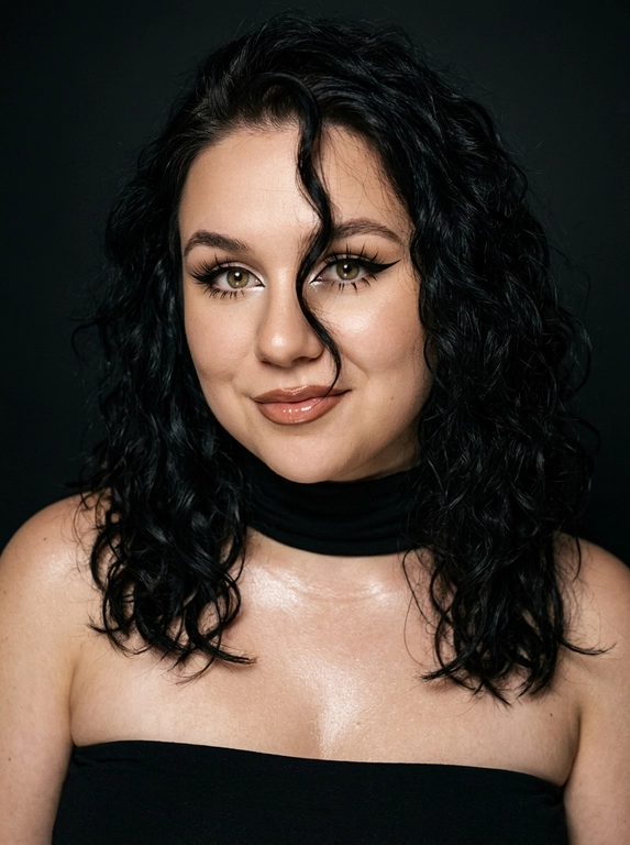 Крупный план лица женщины в стиле «высокой моды». Элегантный макияж: глаза с длинными острыми чёрными стрелками, длинные густые ресницы с эффектом «лучики», нижние ресницы также прокрашены. Хайлайтер во внутренних уголках глаз и на скулах. Губы слегка приоткрыты в лёгкой ухмылке, с лёгким блеском и светло-коричневым карандашом по контуру. Голова наклонена в сторону,  На ней чёрный топ из тканевого материала без бретелек. Тело и зона декольте подсвечены хайлайтером, на шее чёрная ткань. Высокая детализация текстур кожи, одежды и волос. Черты лица полностью сохранены, как на референсном фото. Фон чёрный, студийный, вокруг темнота, лицо освещено яркой лампой. 8K, тёмный минималистичный фон без лишних деталей. Гиперреализм, добавить зерно.

Какая будет прическа?: Волосы густые уложены в пляжные локоны, локон волос падает на лицо.