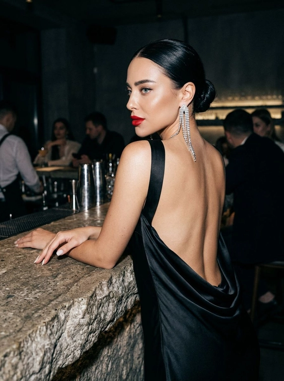 Создай изображение женщины с фотографии, не изменяя лицо, черты, внешность, возраст и индивидуальность. Она в элегантном черном вечернем платье с открытой спиной, ткань подчеркивает тонкую кожу с естественным свечением, складки и блеск шелка придают глубину. Опирается на необработанную каменную стойку с шероховатой фактурой, контрастирующей с платьем и кожей. Приглушенный свет лаунжа создает мягкие тени, подчеркивая изгибы спины и переходы света на платье и камне. Длинная сверкающая диамантовая серьга спускается по спине, ловя свет и создавая мерцание. фото в высоком разрешении с зернистой пленочной текстурой и высоким контрастом, в стиле классического нуара и модной редакционной фотографии, с холодным глубоким визуальным стилем свет усиливают глубину и светотеневой рисунок. Строго сохранить лицо, идентичность и естественную внешность человека с оригинала. Фото в цвете.

Какая будет прическа?: Волосы в гладком пучке без выбившихся прядей, придающем утонченность и сдержанность.