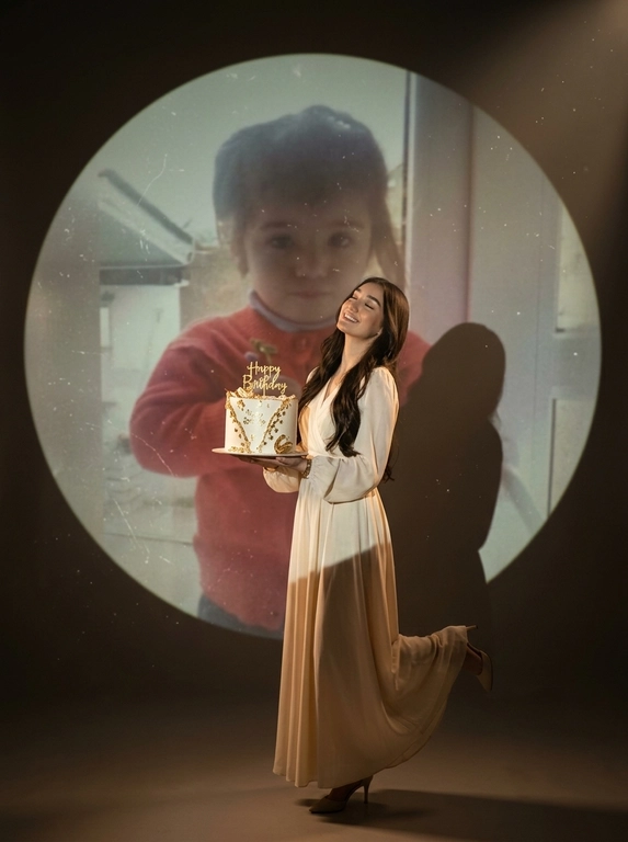 Create ultra-realistic cinematic birthday photoshoot, elegant studio with a dark background and a large circular spotlight projection on the wall. Inside the spotlight, a faded vintage childhood photo of the same girl(the reference image 2nd given)appears as a nostalgic memory, slightly transparent with old photo texture and soft blur. In the foreground, the present-day version of the same model (the reference image 1st given)  holding a white birthday cake decorated with gold accents with a “Happy Birthday". 

If the model is a woman, then she is wearing a cream long gown. If the model is a man, he is wearing a suit.

her head tilted back, eyes closed, natural smile,  cinematic shadow cast on the wall, warm soft spotlight lighting.

If the model was a woman, she additionally lifted her leg in an elegant pose.

Доп. характеристики: 15 лет