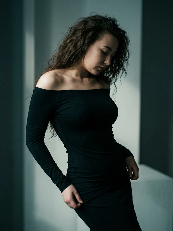 В минималистичной студии женщина в облегающем платье из тонкой ткани с длинными рукавами и спущенным одним плечом плавно выгибает корпус, голова склонена влево и опущена. Одной рукой она тянет подол у бедра. Жёсткий луч света слева подчёркивает ключицы и складки ткани, справа остаётся густая тень. Вертикальный кадр, средний план, лёгкий нижний ракурс, 50 мм, f/2.0.
Цветное изображение с глубокой, тёмной плёночной цветокоррекцией: приглушённые оттенки, холодные тени с лёгким сине-зелёным (teal) подтоном, тёплые, но сдержанные акценты кожи, мягкое выцветание светов, эффект киноплёнки, высокий контраст, деликатное плёночное зерно, кинематографическая атмосфера, 4K.

Какая будет прическа?: Волосы уложены в объёмные небрежные пляжные локоны с мягкой естественной текстурой.

Какого цвета будет платье?: Цвет платья на модели черное.