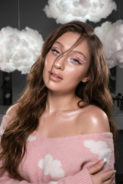 Крупный план лица девушки в стиле «высокой моды». Элегантный макияж глаза с длинными острыми нежно розовые двойные изогнутые стрелки, длинные густые ресницы эффект лучики, нижние густо ресницы накрашены белым и белый каял карандаш на нижнем веке белый Хайлайтер во внутренних уголках и скулах. Губы слегка приоткрыты в легкой ухмылке в легком блеске. Голова наклонена в сторону. На ней пушистый дорогой кашемировый нежно розовый свитер с белыми облаками плечи открыты.
За ней свисают объемные пушистые облака из ваты подсвеченные белым изнутри. Тело и декольте подсвечены хайлайтером и шиммером. Высокая детализация текстур кожи, одежды и волос. Черты лица-полностью сохранены как на референсном фото.
Ногти френч квадрат длинные.
На фоне светлая большая бьюти студия, вокруг темно, ее лицо освещено яркой лампой.  Волосы очень длинные блестящие прическа пляжные локоны. Локон волос падает на лицо 