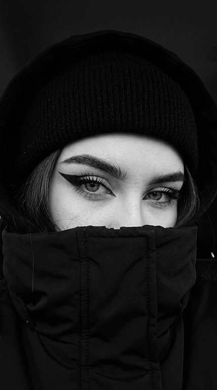 Не меняя внешности женщины с фото, перед нами крупный план её лица, частично скрытого под чёрной шапкой-бини, капюшоном и чёрной курткой с высоким воротом, которые обнимают нижнюю часть лица, оставляя видимыми только выразительные глаза.

Очень близкое селфи на iPhone 16, горизонтальный кадр, видно только глаза и брови, взгляд направлен прямо в камеру. Фото цветное, сильно затемнённое, с глубокими тенями, мягким контрастом и холодной приглушённой цветокоррекцией. Чёрные элементы одежды остаются насыщенными и глубокими, кожа сохраняет естественный оттенок без пересветов и искусственного сглаживания.

Веки полуприкрыты, создавая томный, тяжёлый и дерзкий взгляд. Стрелки большие, острые, дерзкие, с чёткими графичными линиями. Ресницы длинные и пушистые. Брови строго очерчены и подчеркнуты тёмным оттенком. Взгляд направлен прямо в камеру, создавая атмосферу загадочности и напряжённости.

Свет падает мягко и равномерно, но остаётся очень приглушённым, делая главный акцент на глубине взгляда. Волосы, видимые лишь частично, слегка выбиваются из-под шапки.

Фон очень тёмный, приглушённый, с минимальным количеством цветовых деталей и без ярких отвлекающих оттенков. Общая цветовая гамма холодная, глубокая и кинематографичная, с лёгким уклоном в серо-графитовые и нейтральные тона.

Стиль кадра кинематографичный, с высокой глубиной теней, реалистичной текстурой кожи и ткани, без глянцевой ретуши, без эффекта пластика и без ИИ-сглаживания. Фотореалистичное изображение, высокая текстурная детализация, разрешение 8K. Фото снято на iPhone 16.


Фото в чёрно-белом или в цвете?: Стиль кадра чёрно-белый