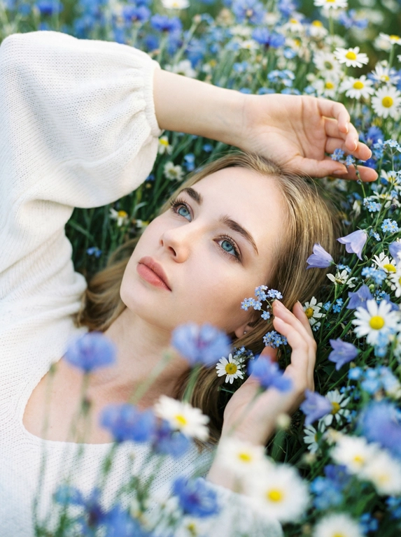 Экстремально крупный, кинематографичный портрет лица человека, лежащего среди густых полевых цветов, камера максимально близко — в кадре преимущественно лицо, черты сохранены без изменений, вокруг море цветов, создающее ощущение мягкого природного кокона, одна рука изящно поднята над головой, вторая мягко касается цветов рядом, на переднем плане сбоку частично размытые, не в фокусе цветы добавляют глубину и лёгкое ощущение движения, одета в летнее белое вязаное платье с объёмными рукавами, мягкая текстура ткани едва читается, естественный мягкий свет подчёркивает кожу и блики в волосах, малая глубина резкости, художественное боке, атмосферный кадр с деликатным плёночным зерном.



Какие будут цветы?: Цветы нежно-голубых, синих и белых оттенков.