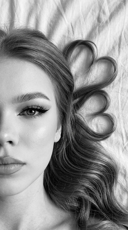 Фото снято на фронтальную камеру iPhone 16 Pro Max. Фотореалистичное чёрно-белое селфи девушки, лежащей на светлой слегка смятой простыне. крупный план. Камера расположена прямо над лицом. В кадре видна только половина лица, один глаз смотрит прямо в камеру.

Макияж выразительный и аккуратный, в эстетике clean soft glam: чёткие графичные чёрные стрелки с вытянутым эффектом, длинные густые ресницы с лисьим эффектом, хорошо оформленные брови с аккуратной укладкой наверх, мягкий контуринг, деликатный хайлайтер во внутренних уголках глаз, на скулах и спинке носа, губы с чётким контуром и мягким гладким финишем. Макияж выглядит безупречно, дорого и очень чисто.

Волосы естественно уложены на одну сторону вокруг головы, две крупные пряди случайно образуют два сердца, остальные волосы свободно и натурально лежат волнами. Мягкий естественный дневной свет из окна, лёгкие тени. Высокая детализация лица, чётко видны поры кожи, текстура губ, ресницы, брови и отдельные волоски. Волосы максимально детализированные, с естественным блеском и объёмом. Минималистичный кадр, светлая ткань с натуральными складками на фоне, без лишних предметов. Фото снято на фронтальную камеру iPhone 16 Pro Max.

Доп. характеристики: Ровное лицо，без прыщей