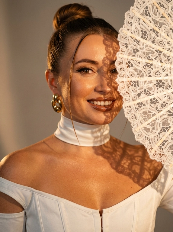 Ultra realistic beauty editorial portrait. Крупный портрет модели: лицо, шея и плечи, лёгкий наклон камеры. Белый кружевной веер частично закрывает лицо, создавая чёткие lace shadows на щеке, глазе, шее и ключице.
Белый структурный корсет с открытыми плечами и плотный satin neck wrap, плотно облегающий шею.  Макияж: sharp eyeliner, длинные ресницы, glossy brown lips, сияющая бронзовая кожа с натуральной текстурой.
Тёплый направленный свет, глубокие тени, золотистый glow, крупные золотые серьги, cinematic contrast, subtle film grain, Vogue aesthetic, RAW realism, ultra detailed 8K, no plastic skin.

Какая будет прическа?: Волосы — sleek high bun с тонкой прядью у лица.

Доп. характеристики: Лицо молодое. Улыбается
