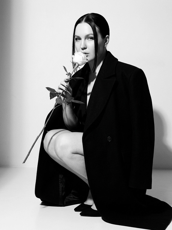 Высоко модная черно-белая редакционная фотография женщины в эффектной позе. Она грациозно присела на корточки, накинув на плечи объемное структурированное черное пальто, оставляя ноги открытыми.
Держит в руке белую розу с длинным стеблем и листьями, поднося к губам бутон. Изящный, минималистичный стиль. Сильное направленное студийное освещение, создающее глубокие тени и высокий контраст. Изысканный макияж с четкой подводкой для глаз и блеском на губах. Чистый фон, эстетика роскошного журнала, стиль Vogue, сверхчеткая, высококонтрастная монохромная фотография. Не изменяйте и не модифицируйте структуру лица, тон кожи или пропорции тела модели.
Только освещение, фон и застывшие текстуры должны быть переосмыслены в контексте задания. Сверхчеткое изображение, высокий динамический диапазон, студийная четкость, реалистичная текстура кожи, естественные поры, едва заметная зернистость пленки, редакционная цветокоррекция, съемка для печати.

Какая будет прическа?: Волосы гладко собранные назад волосы, две прямые пряди спереди выпущены.