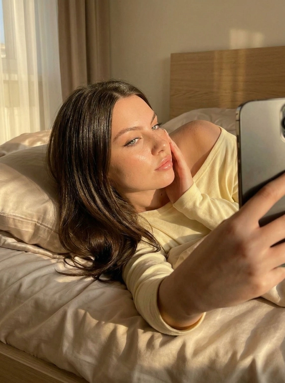 Не меняя черты лица Создай портрет, не меняя черты лица. Девушка лежит на кровати делая селфи от первого лица, она в нежно желтом лонгсливе, спущенном с плеча
Волосы цвет как на фото длинные распущенные блестящие лежат на подушке, голова полубоком.
Постель  светло бежевая сатиновая, фото в золотой час
Солнце красиво освещает её лицо, её безупречный макияж.