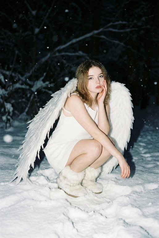  Создай фото человека на основе загруженной фотографии.
Белое платье без рукавов, пушистые белые сапоги, большие белые крылья, опущенные вниз, шире плеч.
Сидит на корточках на снегу, рукой касается щеки. На заднем плане заснеженный лес.
Ночная улица, тёмный размытый фон, вспышка.
Мягкое нечеткое фото: шум, зерно, лёгкое размытие, холодная атмосфера.