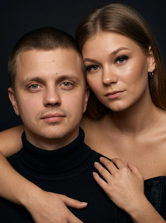 Гиперреалистичный студийный fashion-портрет молодой пары по загруженному референсу, 100% сходство лиц. Черты лица не изменять. Крупный план, кадр по плечи. Мужчина, спокойный уверенный взгляд прямо в камеру, естественное выражение лица, одет в черный трикотажный свитер с высоким воротом. Женщина стоит позади мужчины и нежно обнимает его, ее руки лежат на его плечах. Ее лицо расположено рядом с его лицом, она повернута слегка боком, голова немного наклонена вперед, взгляд направлен прямо в камеру. У женщины выразительные глаза с длинными густыми черными ресницами, естественный clean-glam макияж, натуральные брови, теплый оливковый оттенок кожи, небольшие серьги-кольца. Композиция плотная и интимная, их лица расположены очень близко друг к другу, современный модный портрет пары. Женщина одета в черный корсет. Кожа максимально натуральная: живая текстура кожи, видимые микропоры, subtle skin glow, естественный мягкий блеск кожи, natural skin microtexture, skin translucency, micro skin details, легкие естественные несовершенства кожи, без ретуши и без эффекта пластика. Освещение: мягкий студийный beauty lighting, рассеянный ключевой свет спереди и немного сбоку, мягкие глубокие тени для объема лица, деликатные световые блики на коже. Фон: глубокий темный студийный фон, темно-графитовый или почти черный, создающий контраст с кожей и лицами. Стиль: luxury fashion editorial photography, high fashion portrait, ultra photorealistic, 85mm portrait lens, shallow depth of field, creamy bokeh, cinematic soft lighting, RAW photo, extremely detailed, fine hair strands, natural skin pores, professional photography, photorealism, 8k, high dynamic range.