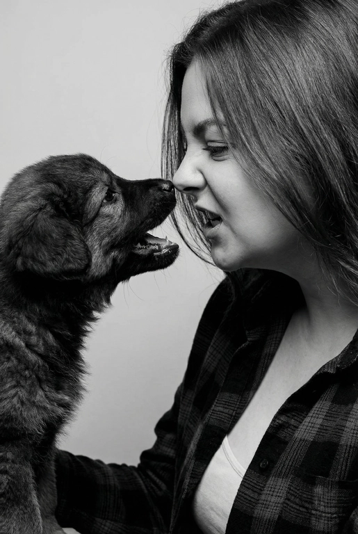 Сделай фото со мной и моим питомцем. Реалистичное фото, с высокой детализацией. Снимок меня и моего питомца в профиль. Фото сделано первым средним планом (Medium CloseUP), в кадре видно часть туловища (с головы до середины груди).
Я стою лицом к своему питомцу в строгий профиль, смотрю прямо на него.
Мой питомец расположен прямо напротив моего лица, также в профиль, смотрит прямо на меня. Наши носы почти соприкасаются. Наши головы могут быть наклонены: например, моя голова наклонена немного вниз, а голова питомца наоборот повыше. Четкая визуальная симметрия между моем лицом и головой моего питомца.
Студийное освещение, мягкий свет, создающий контрастность и скульптурные тени, на самом лице минимум тени. 
 Я и питомец игриво рычим.  Черно-белая фотография. Фон светлый, нейтральный. 