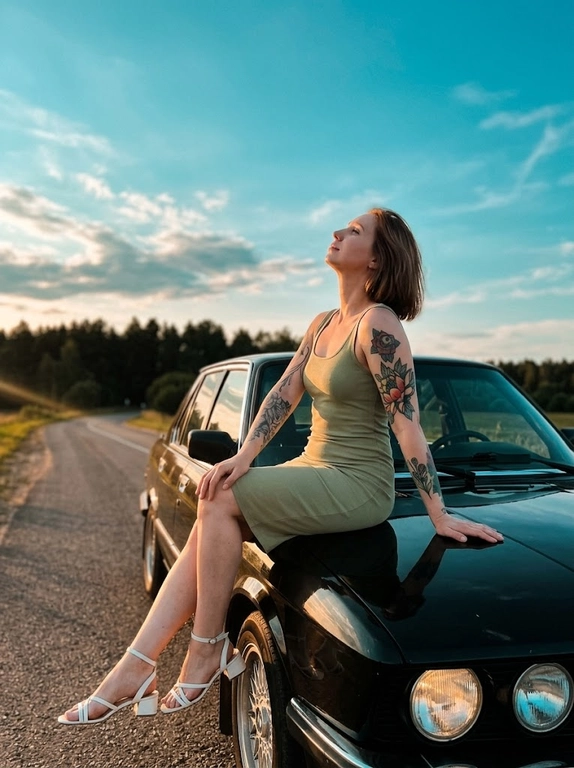 Модель в светло-оливковом платье-футляре и белых босоножках на небольшом каблуке с ремешком сидит боком на краю капота машины.  Кадр в «золотой час» на загородной трассе. Расслабленная поза, голова запрокинута, взгляд вверх.
Освещение теплое закатное, с золотистыми бликами и выраженными тенями. Фон: бирюзово-голубое небо с большим отрицательным пространством, линия леса.
Кинематографичная тонировка с легким «teal & orange». Атмосфера спокойствия, свободы и летнего вечера. Высокая детализация и фотореализм.

Какая будет машина?: BMW черный