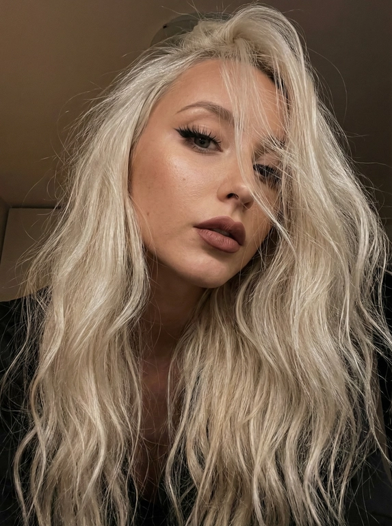   
Крупный план (selfie-style) молодой женщины с эффектной внешностью. У неё очень длинные, густые, слегка волнистые светлые волосы, которые хаотично спадают на лицо. Черты лица выразительные: полные губы с матовой помадой приглушенного розово-коричневого оттенка. Макияж: стрелки, длинные выразительные ресницы, кожа с натуральной естественной текстурой.
Ракурс и композиция:
Снимок сделан снизу вверх под углом (голова наклонена). Лицо занимает большую часть кадра, взгляд направлен в камеру, создавая загадочную атмосферу. Часть лица скрыта за прядями волос.
Освещение и цвета:
Приглушенное, теплое комнатное освещение. Источник света находится сверху, создавая мягкое сияние на коже и контурный свет на волосах. Цветовая гамма темная, с преобладанием глубоких черных, телесных и теплых бежевых тонов.
Стиль:
Эстетика "Instagram selfie", высокое качество, эффект мобильной фотографии с легким естественным зерном, мягкий фокус.
Высокая детализация текстур кожи и волос. лица-полностью сохранены как на референсном фото.
размер 9:16.
