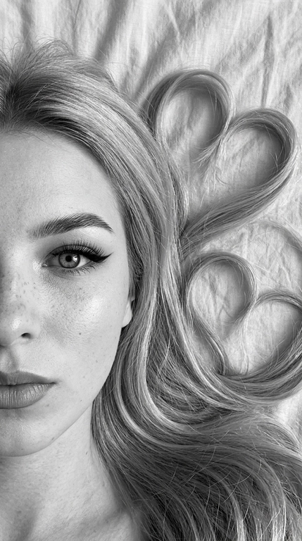 Фото снято на фронтальную камеру iPhone 16 Pro Max. Фотореалистичное чёрно-белое селфи девушки, лежащей на светлой слегка смятой простыне. крупный план. Камера расположена прямо над лицом. В кадре видна только половина лица, один глаз смотрит прямо в камеру.

Макияж выразительный и аккуратный, в эстетике clean soft glam: чёткие графичные чёрные стрелки с вытянутым эффектом, длинные густые ресницы с лисьим эффектом, хорошо оформленные брови с аккуратной укладкой наверх, мягкий контуринг, деликатный хайлайтер во внутренних уголках глаз, на скулах и спинке носа, губы с чётким контуром и мягким гладким финишем. Макияж выглядит безупречно, дорого и очень чисто.

Волосы естественно уложены на одну сторону вокруг головы, две крупные пряди случайно образуют два сердца, остальные волосы свободно и натурально лежат волнами. Мягкий естественный дневной свет из окна, лёгкие тени. Высокая детализация лица, чётко видны поры кожи, текстура губ, ресницы, брови и отдельные волоски. Волосы максимально детализированные, с естественным блеском и объёмом. Минималистичный кадр, светлая ткань с натуральными складками на фоне, без лишних предметов. Фото снято на фронтальную камеру iPhone 16 Pro Max.